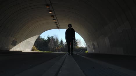 silhouetted figure walking in tunnel with clear sky, conveying a sense of contemplation or travel, daytime