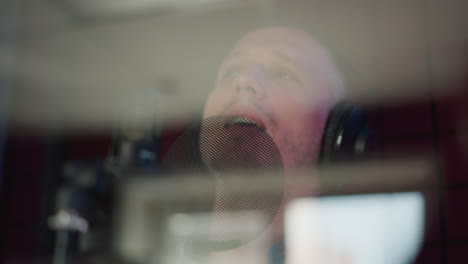 close-up of a man singing into a microphone while wearing black studio headphones. his face is partially obscured by the microphone pop filter, capturing the intensity and focus of his performance