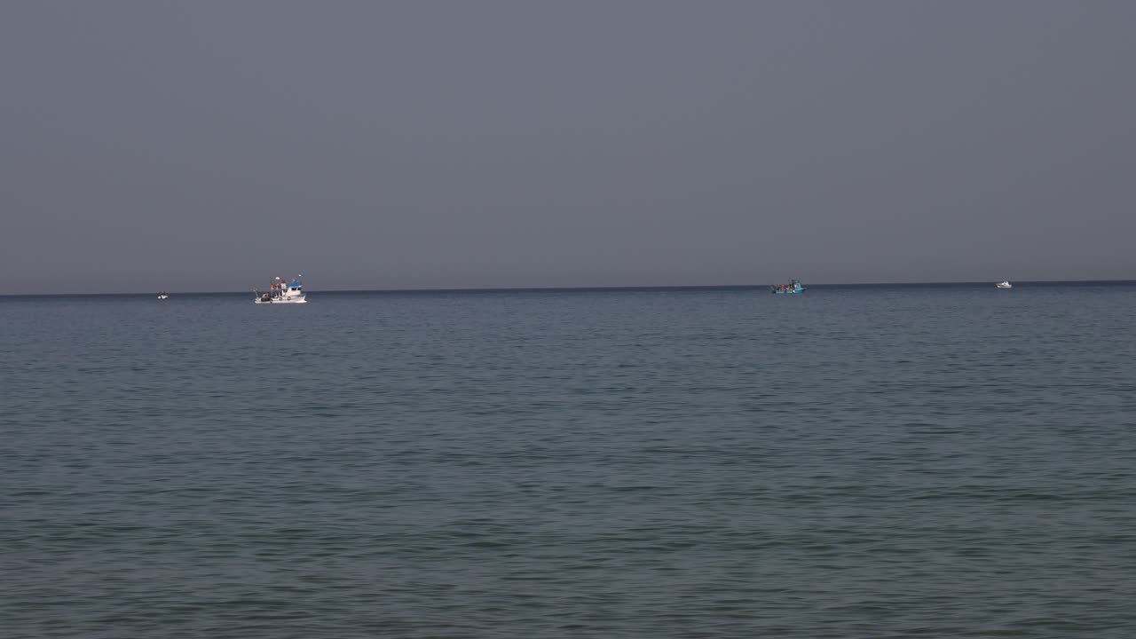Ship sailing on distant calm sea under gray sky during evening light