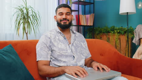 Young-man-freelancer-sitting-on-couch-closing-laptop-pc-after-finishing-work-in-living-room-at-home