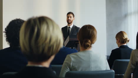 vista trasera de personas sentadas en una sala de conferencias que escuchan a un hombre de negocios caucásico hablando con confianza y emoción