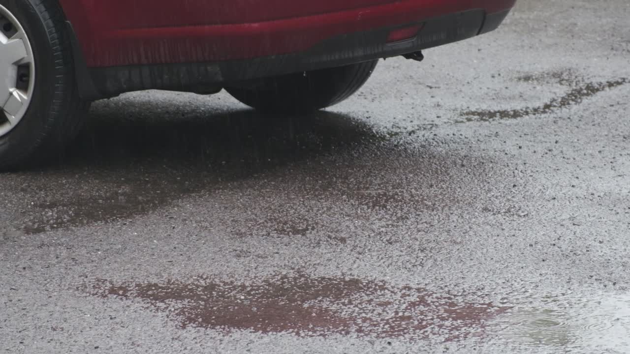 Regnvandspyt med refleksion af rød bil på en parkeringsplads