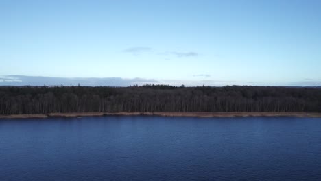 birdseye view of the shoreline of a epic lake with forest in the background - truck shot
