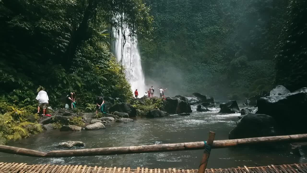 Bali, Spring 2020 in 1080 60p, Daytime, cinematic drone flight Long slow motion flight to the waterfall over the river to a small group of tourists over an indigenous bridge