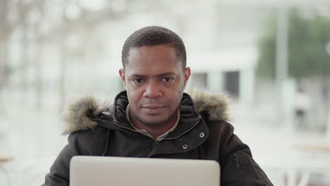 Afro-American-middle-aged-man-in-black-jacket-with-fur-hood-working-on-laptop-outside