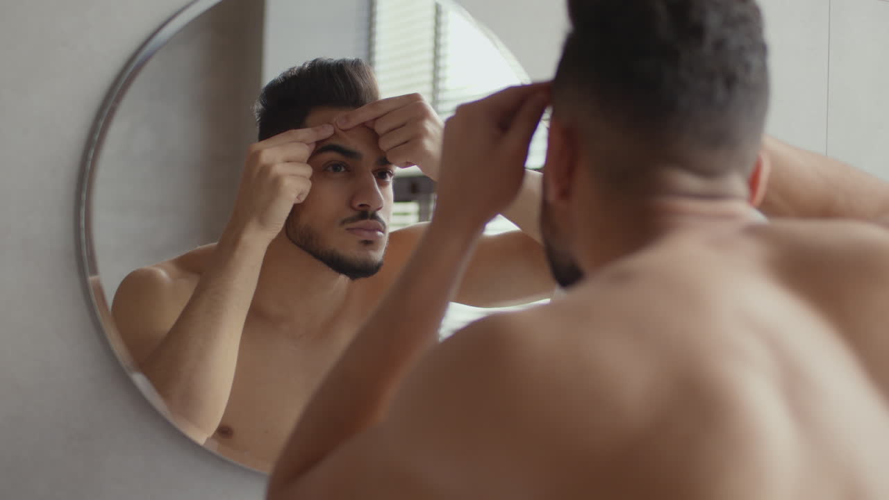 Man checking his face in the mirror for pimples
