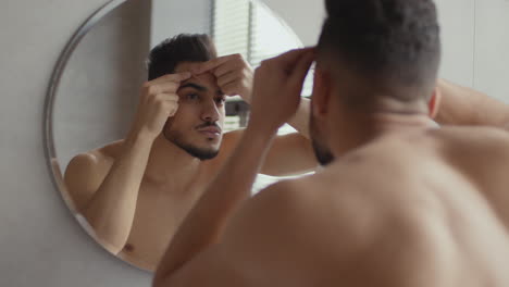 man checking his face in the mirror for pimples