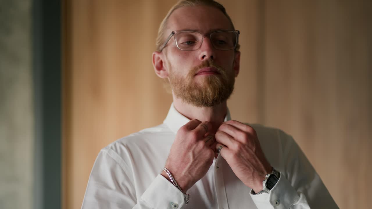 Close-up shot of a confident blond man with glasses in a white shirt looking to the side and straightening his clothes before starting a working day in the office
