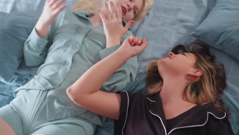 teen girl lies on cozy bed with raised hand, singing passionately in excitement while looking upward, partial view of another person in pajamas beside her adds context to relaxed
