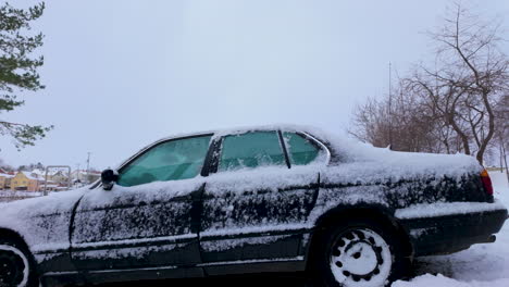 coche cubierto de nieve, estacionado en un paisaje de invierno rodeado de árboles desnudos, reflejando las condiciones climáticas frías