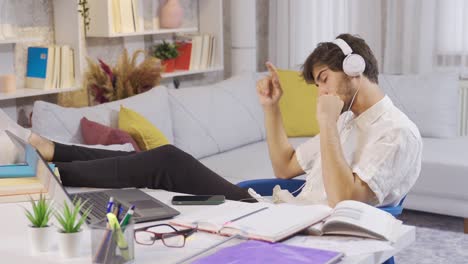 carefree relaxed male student listening to music at his desk at home and enjoying himself.