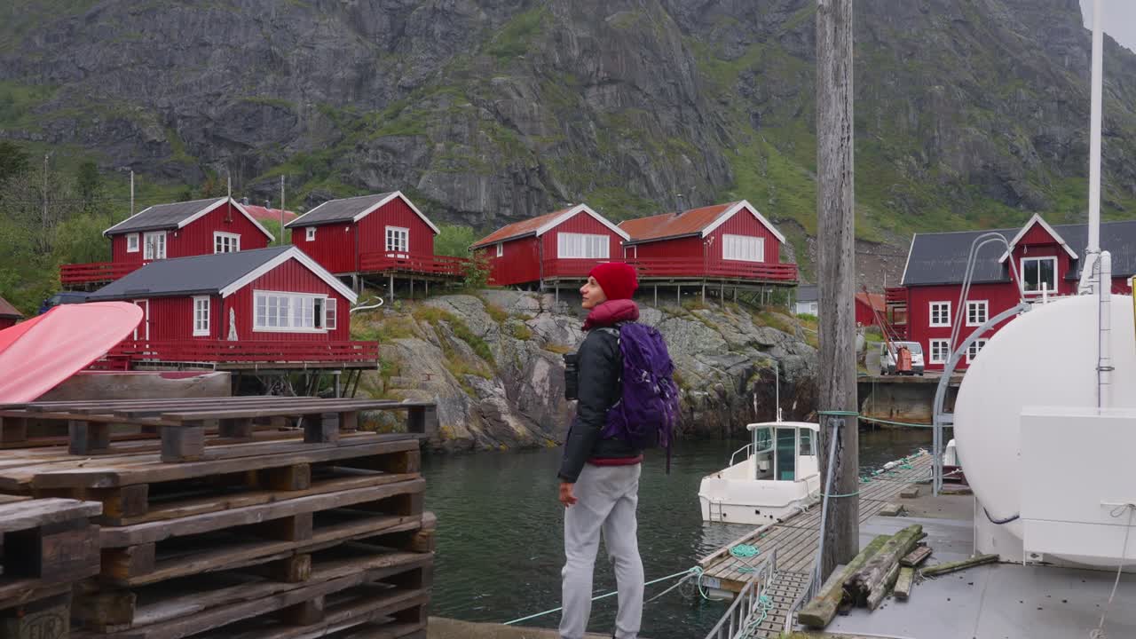 fotografía en cámara lenta de una joven fotógrafa turista admirando el hermoso pueblo de pescadores de å y sus casas de rorbu rojas en las islas lofoten, noruega