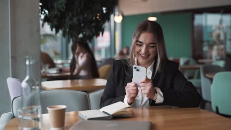 retrato de una joven y hermosa mujer en un café, vestida con ropa de negocios, recibe un mensaje alegre sobre ganar, dinero y victoria