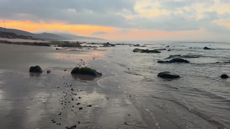 la escena cinematográfica de caminar solo en la playa cerca de las olas del mar salpicando la orilla en la hora de la noche, revelando era la superficie del océano