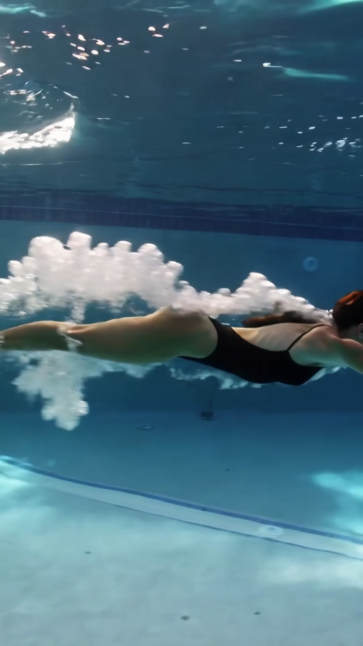 Vertical video: Diving swimmer entering water, gliding at pool in black swimsuit leaving bubbles