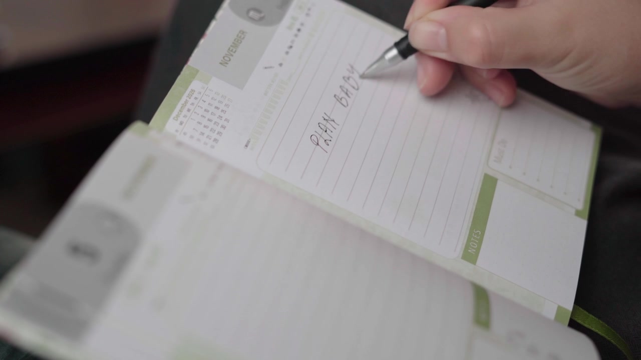 Una donna scrive gli impegni per la festa del bambino in un'agenda settimanale di novembre, organizzando a mano una lista di cose da fare per un baby shower.