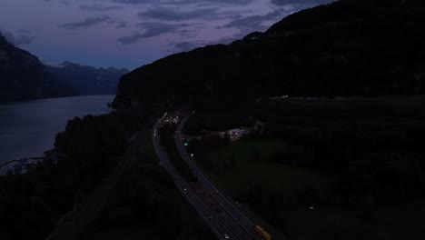 nighttime aerial view of a highway with moving traffic near lake walensee, switzerland, surrounded by serene waters and illuminated by city lights, creating a peaceful evening atmosphere.