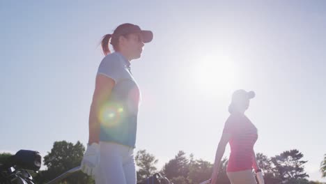 two female caucasian golf players walking with their golf kit carts on the golf course