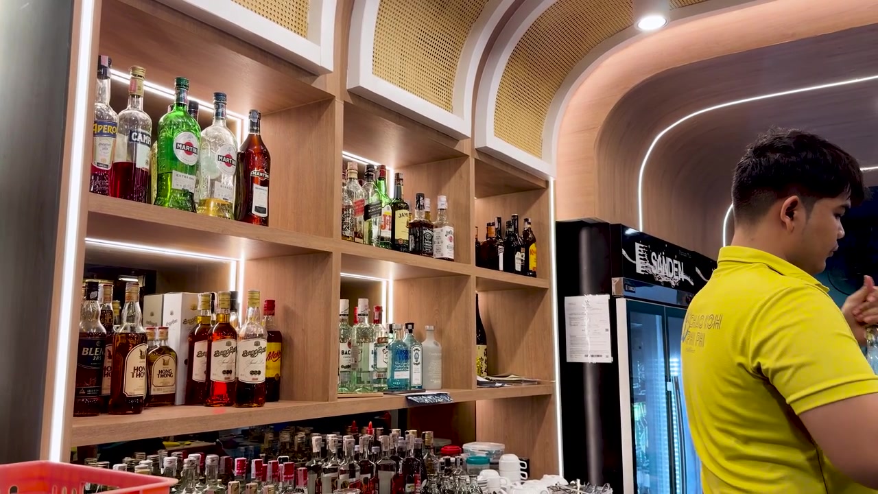 Un barman organiza varias botellas de alcohol en estantes de madera en un moderno bar tailandés