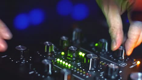 close up view of dj's hands turning knobs on the audio mixing panel with colorful lights flashing - handheld