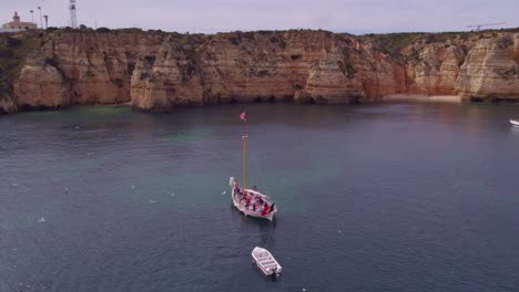 Sail-boat-anchored-near-Ponta-da-Piedade-Lagos-Portugal-during-a-cloudy-day,-aerial