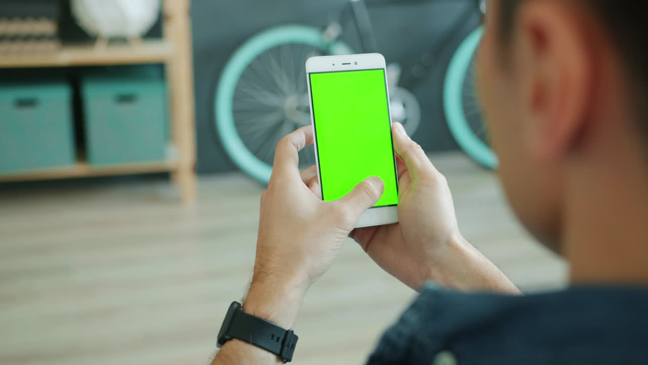 Back view of man using smartphone with green chroma key screen holding modern device