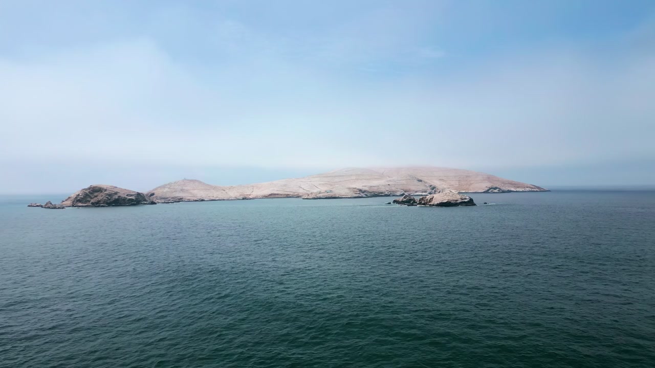 Riprese aeree orizzontali con drone che volano in avanti sull'Oceano Pacifico verso un gruppo di isole rocciose al largo vicino a Lima, Perù. Acque di un blu profondo e un approccio cinematografico fluido