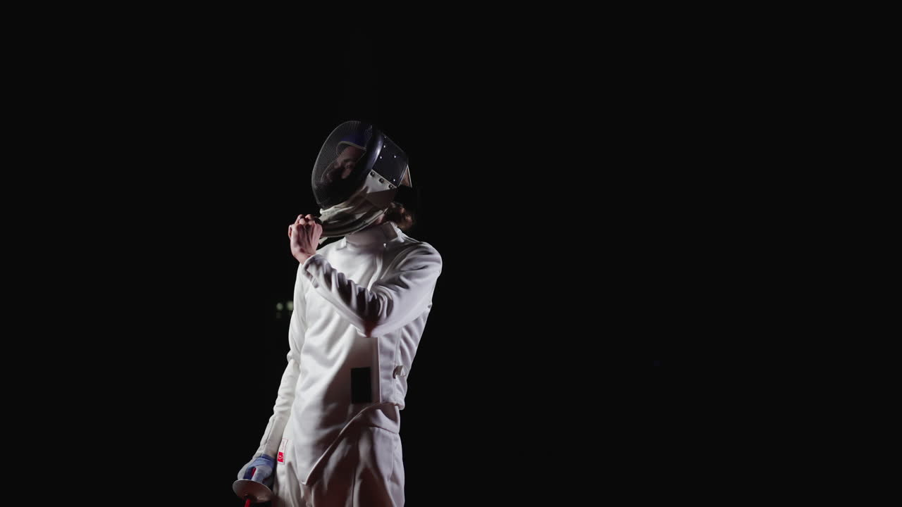 A young man in a fencing uniform, holding a sword, and looking up