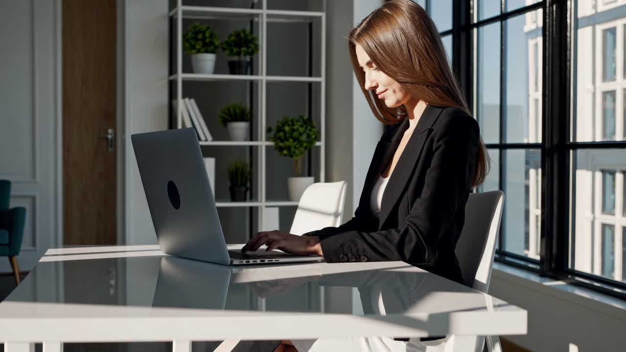 Profesjonalna kobieta pracuje na laptopie w jasnym biurze. Ujęcie z boku ukazuje jej skupienie.