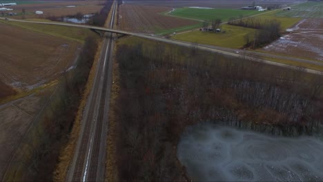 Cars,-trucks-and-a-bus-traveling-across-an-overpass-running-over-railroad-tracks-next-to-a-pond-on-a-rural-Illinois-highway