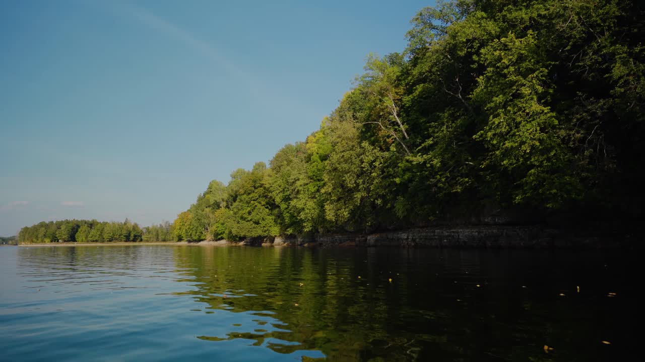 Driving a boat near the river coast with green trees in sunny summer day.
