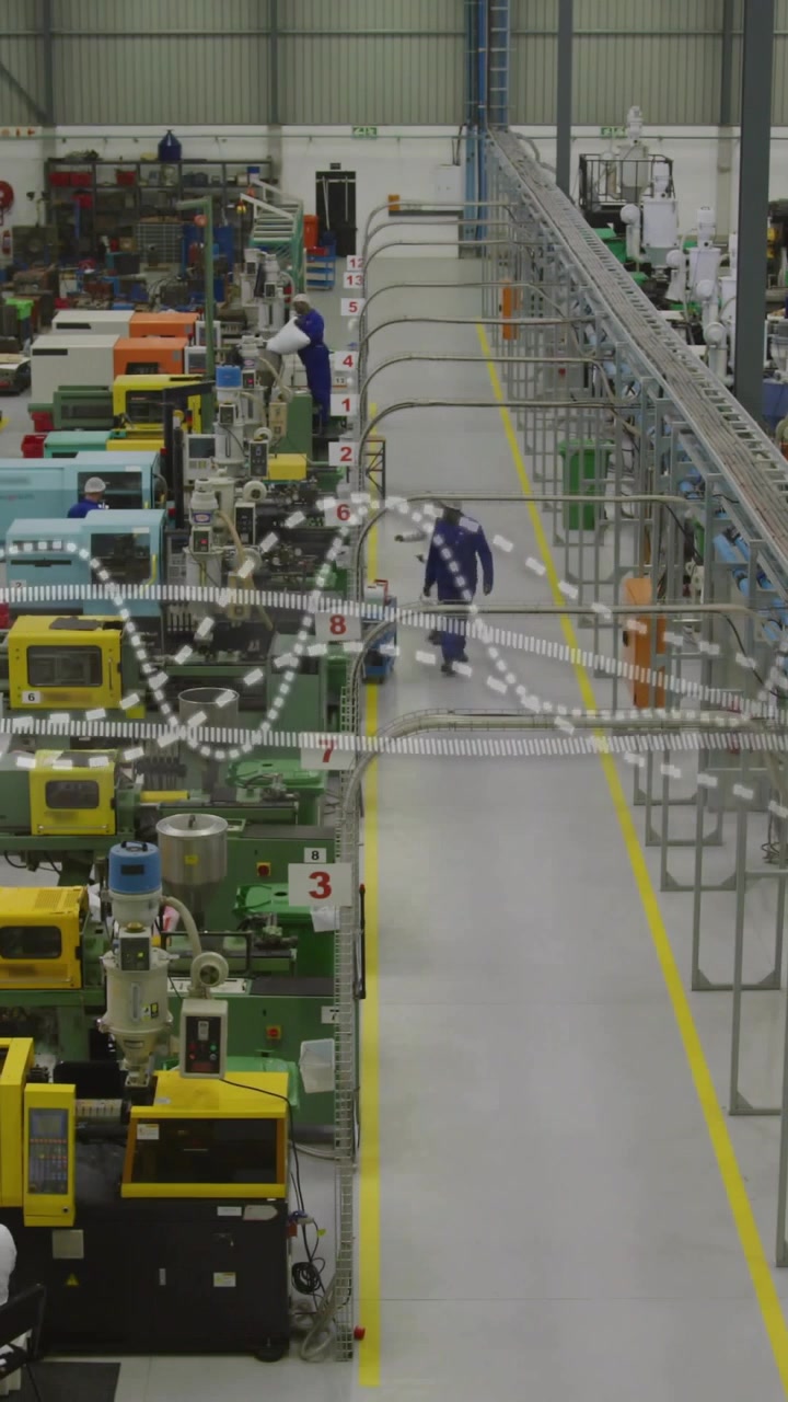 Video vertical: Trabajador apareciendo desde el fondo y caminando por un pasillo de fabricación, inspeccionando estaciones.