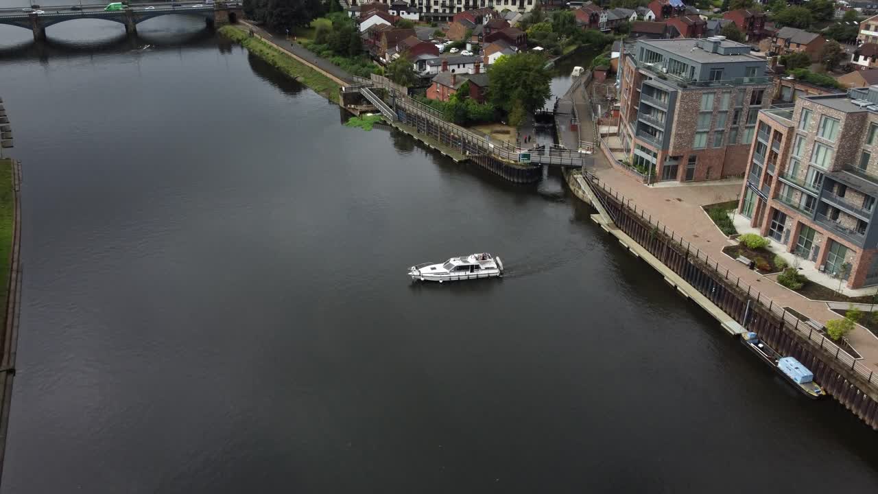 erial footage of a River Boat that has just left the Canal Lock and in on the River Trent heading towards a City Road Bridge, Lon Road. The drone flies up and backwards revealing more of the City.
