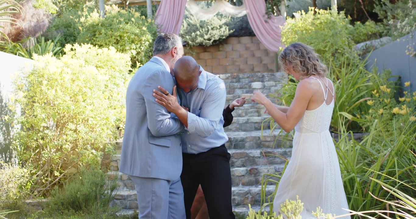 Amici diversi che si salutano sotto una pergola rosa, un uomo che porge la mano, stringendosi la mano, abbracciandosi, ballando.