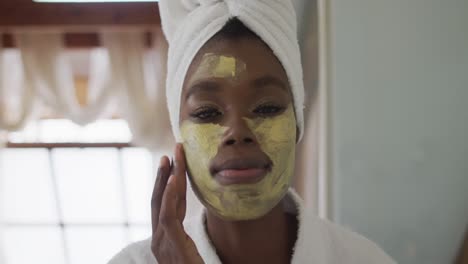 portrait of african american attractive woman applying face mask in bathroom