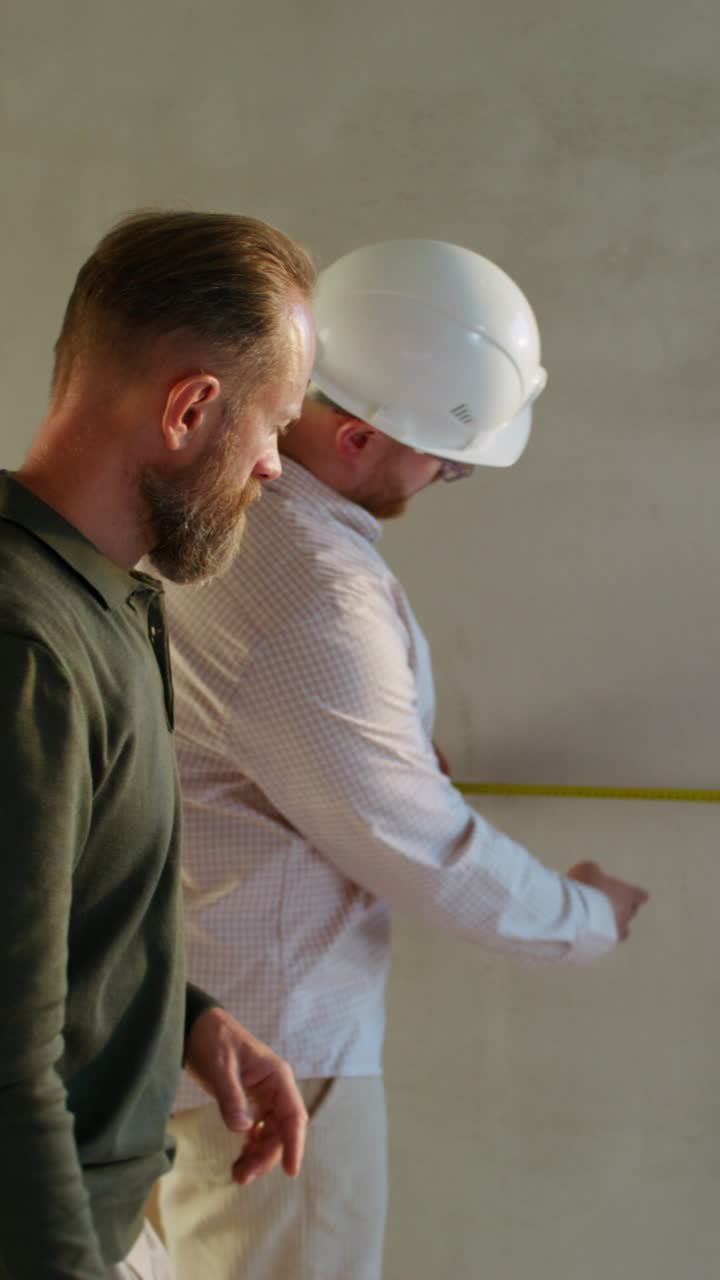 Construction Workers Measuring Wall Using Blueprint