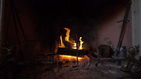 lit fireplace with burning logs, glowing embers, and tools in warm cozy setting