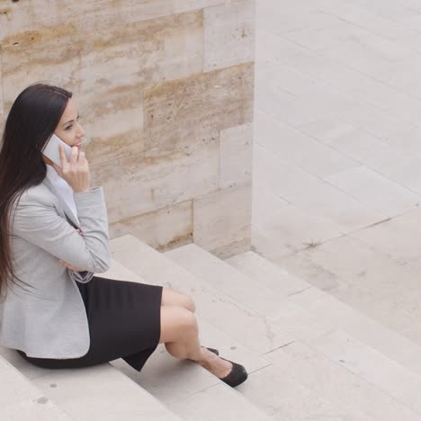 Cute-business-woman-sitting-on-steps-with-phone