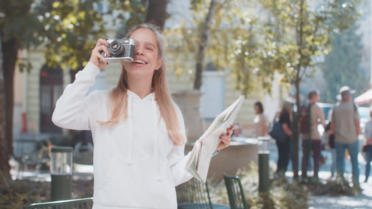 백인 젊은 여성 관광객이 도시 지도를 보고 레트로 빈티지 카메라로 사진을 찍습니다.