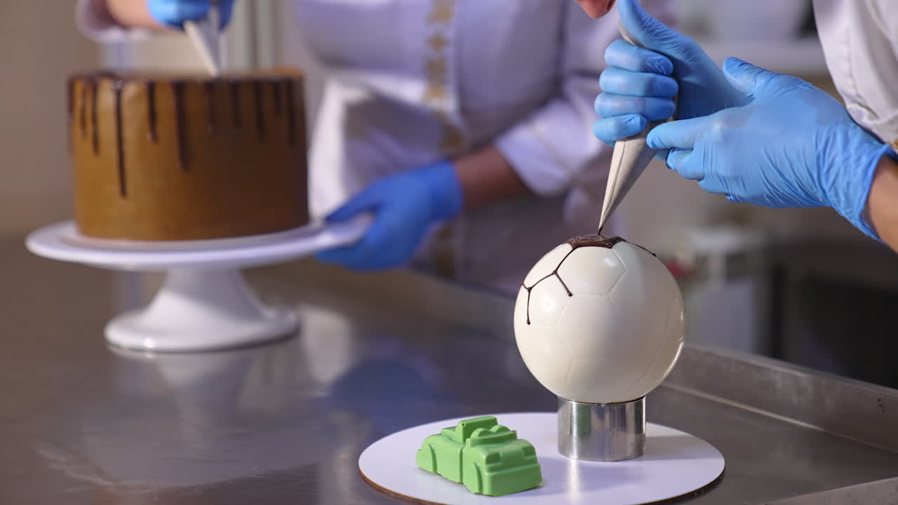 Confectioners decorating cakes in the confectionary. Two cooks working with sweets at the metal table. Blurred backdrop.