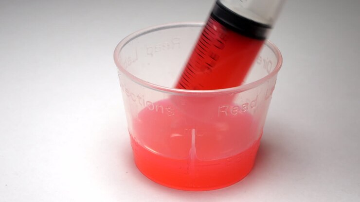 Farmaco antibiotico rosa aspirato in una siringa da un misurino di plastica trasparente.