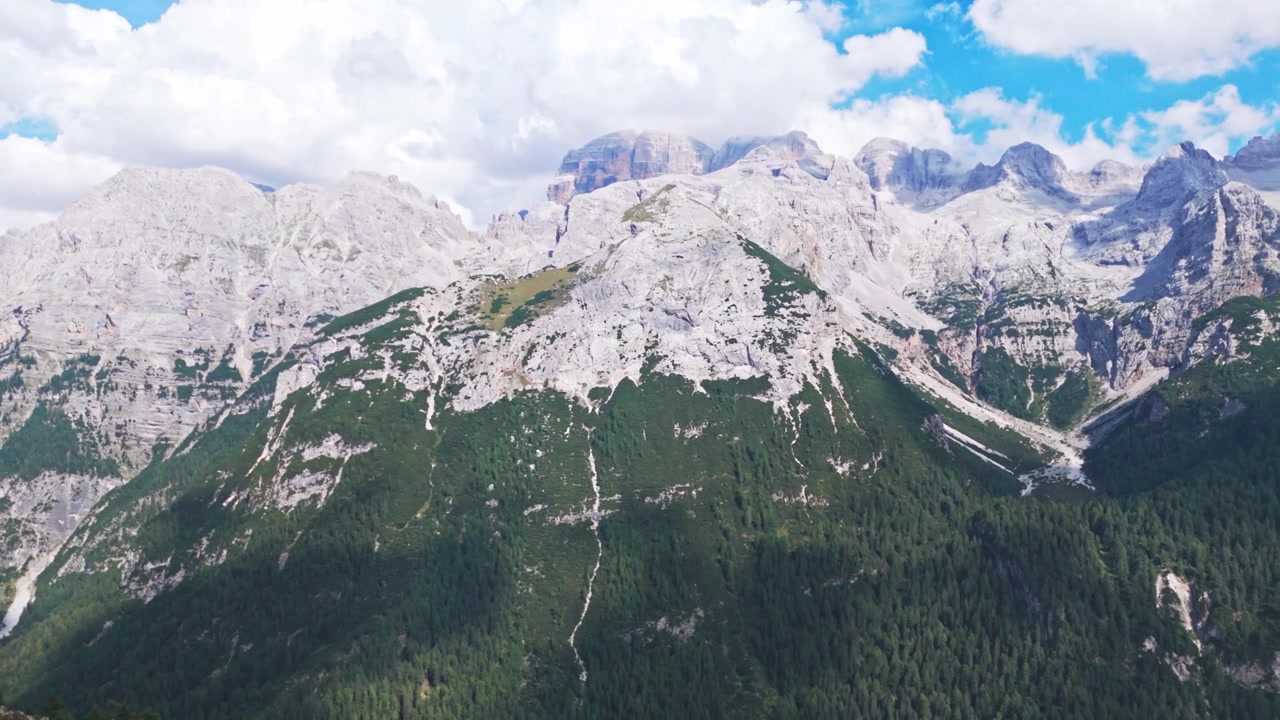 Majestätisk flygvy över Brenta Dolomiternas bergskedja, med klippiga toppar och frodiga gröna skogar under en delvis molnig himmel i Trentino.