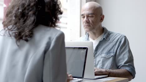 Two-confident-people-sitting-at-table-and-using-laptops