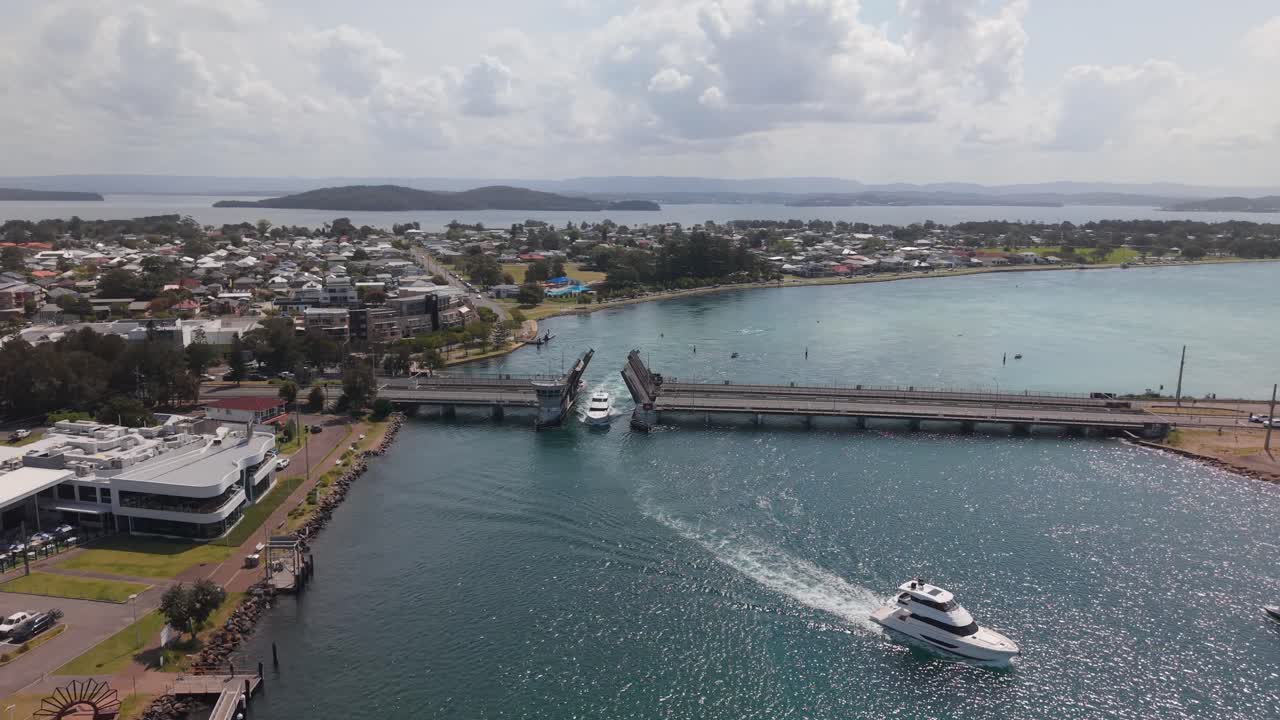 Overhead drone of boats moving under raised bridge on calm water in Swansea traveling out into channel