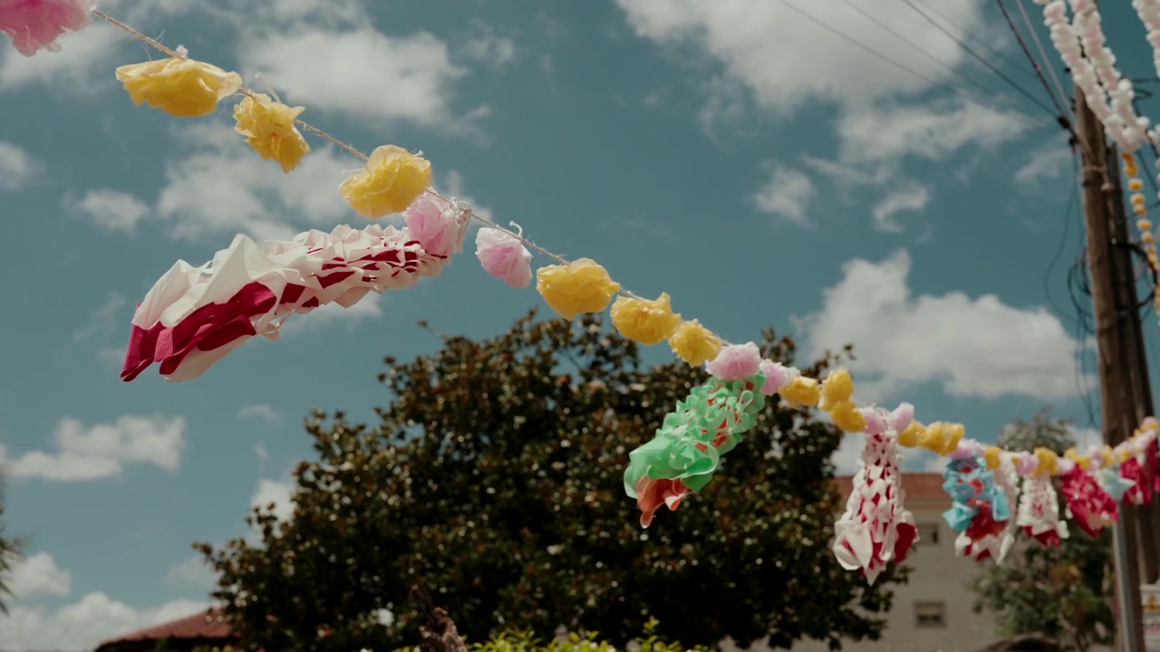 Decorazioni di carta gialle, rosa e verdi appese per strada sopra la cima degli alberi e le case durante un festival arraial