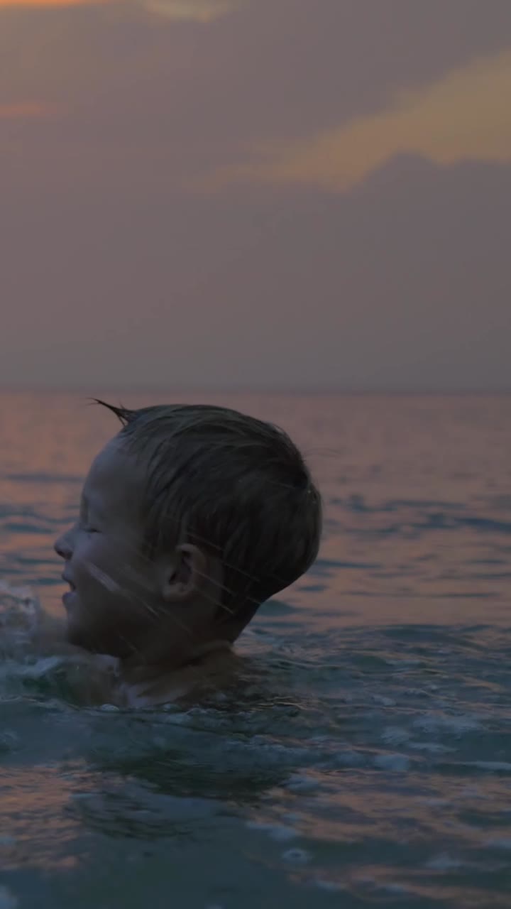 Young Boy Splashing Water in the Ocean at Sunset