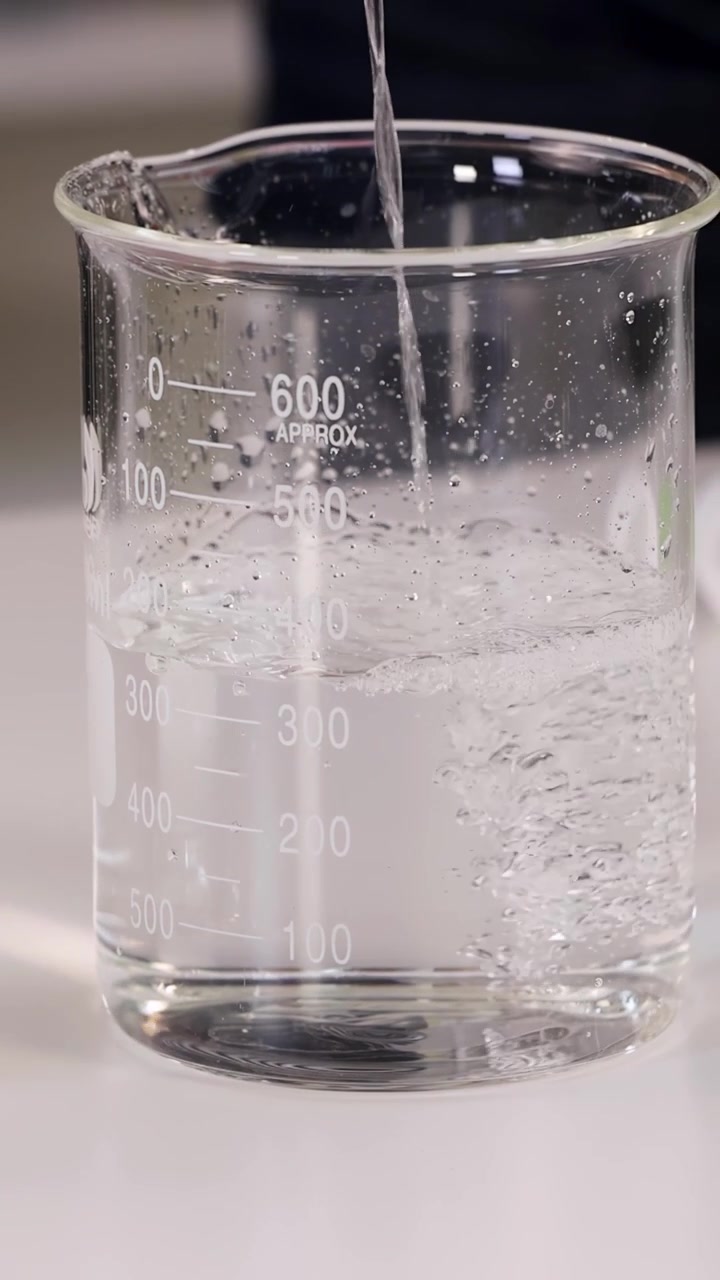 Primo piano di acqua che si versa in un becher di vetro graduato, creando bolle in un laboratorio luminoso
