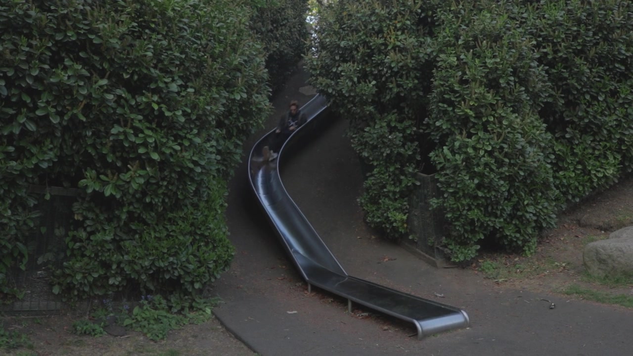 Handheld View of Man Sliding Down Playground Slide in London Park Fun Lifestyle