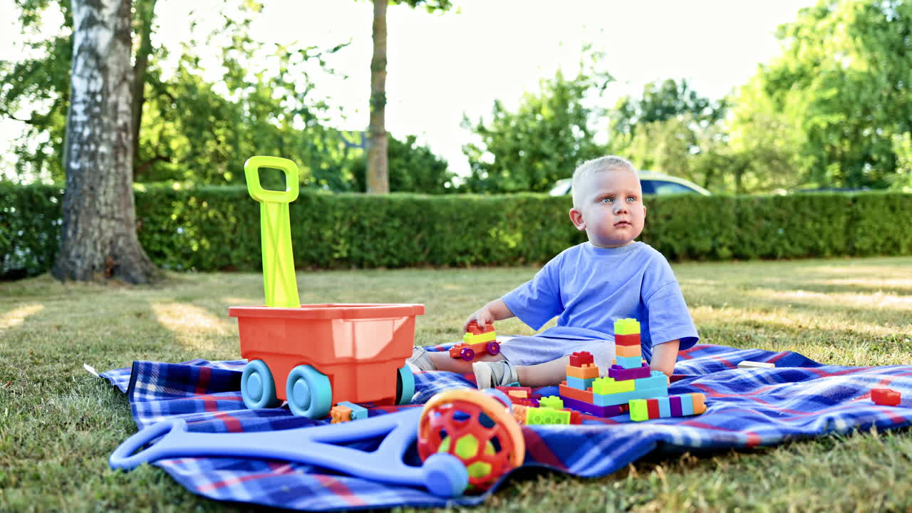 A little boy in a T-shirt and shorts sits on the grass outside and plays with a construction set. A child plays on a swing on a warm sunny day. Child development