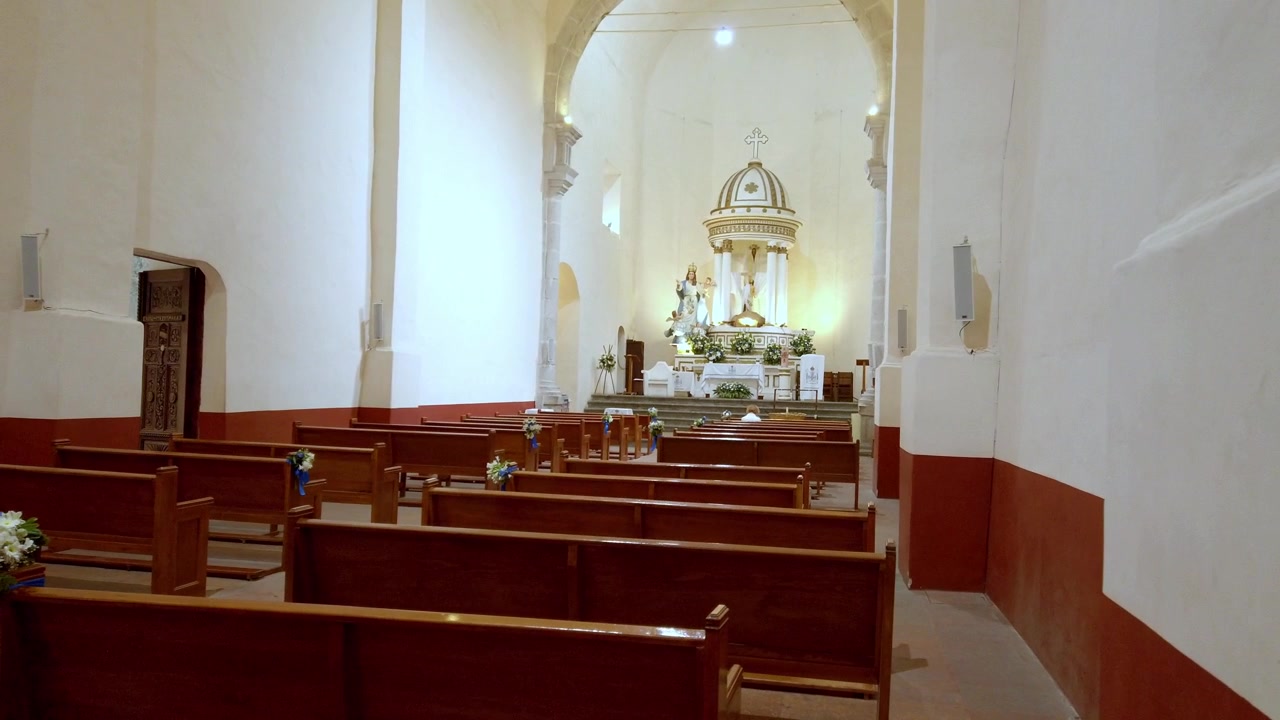 Vista interior de iglesia con filas de bancos de madera frente a un altar decorado bajo un alto techo abovedado dentro de un tranquilo y histórico recinto religioso